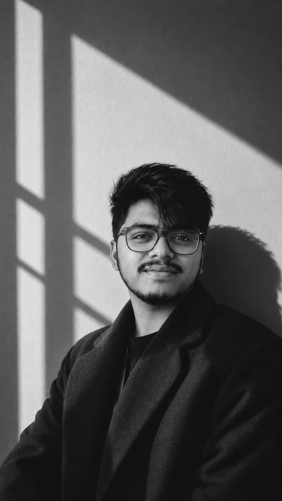 Tamal Biswas in a dark coat, against a wall in hard window light